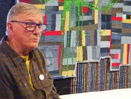 A photo of Bill Stearman in front of a quilt.